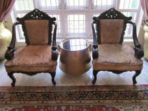 Two old Portuguese chairs restored .One old brass vessel with glass top positioned as tea table, Two huge brass Gangalams serve as curtain holders