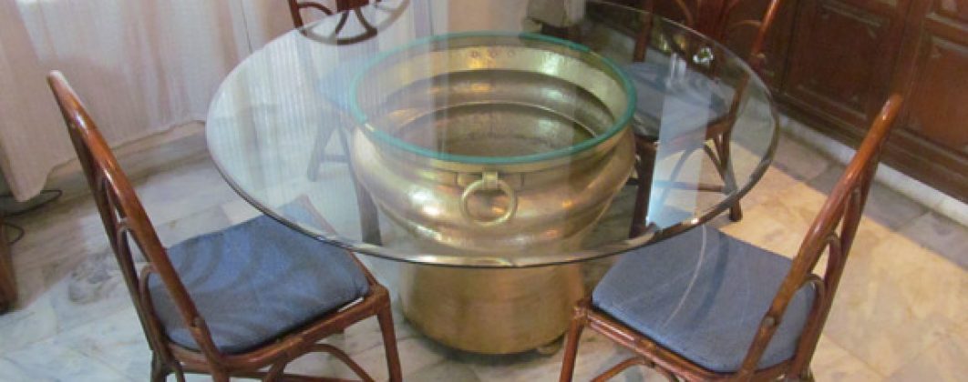 Huge antiques brass gangalam that  serves as a base of the dining table with a glass top